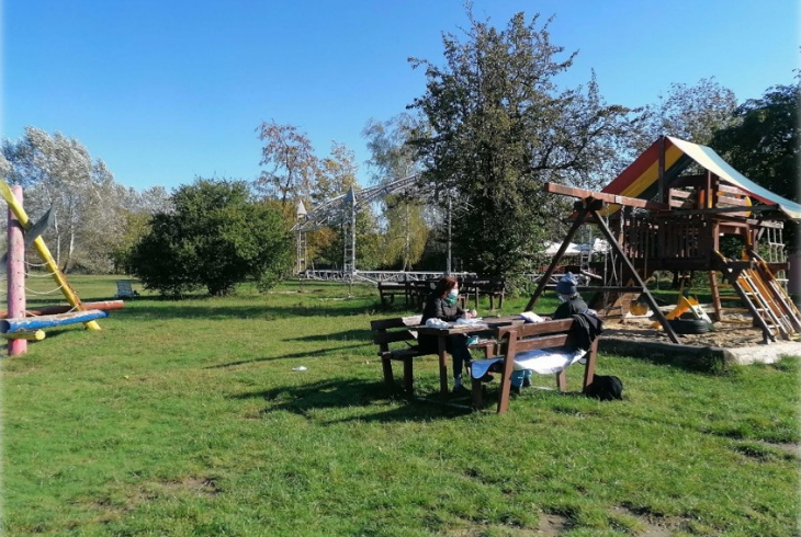 Dvaja ľudia sedia oproti sebe pri stole vedľa detského ihriska v parku